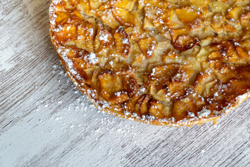 Homemade baking. Freshly baked apple pie on a light wooden background sprinkled with icing sugar.