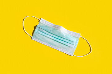 Medical or surgical face mask on a bright yellow background.