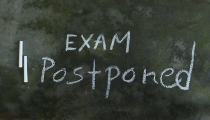 Exam Postponed Written on Blackboard with White Chalk