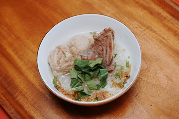 meatball soup with vermicelli and beef ribs. indonesian street food. white bowl. pieces of mustard leaf