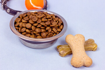 Brown biscuit bones and crunchy organic kibble pieces for dog feed on light blue background. Healthy dry pet food concept.