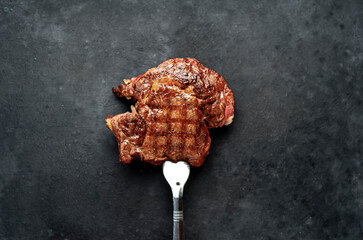 Grilled beef steak with spices on a meat fork on a stone background with copy space for your text.