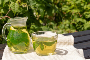 on an old wooden table covered with a white tablecloth, there is a transparent jug and a cup of green tea and blackcurrant and mint leaves