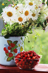 Fototapeta na wymiar A bouquet of daisies and other wild flowers and a bowl with strawberry