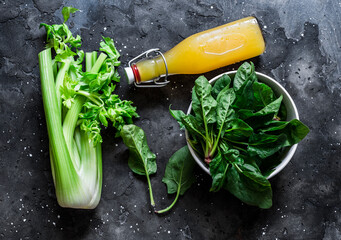 Ingredients for detox diet green smoothies - fresh celery, spinach, natural orange juice on a dark...