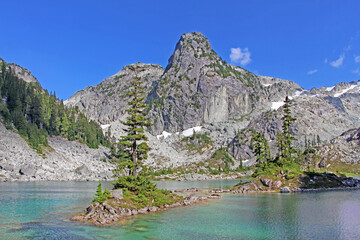 Fototapeta na wymiar Watersprite lake hike near Squamish in BC, Canada. The view on the turquoise lake surrounded by rocky mountains slightly covered with snow. Little island in the middle of lake with green pine tree.