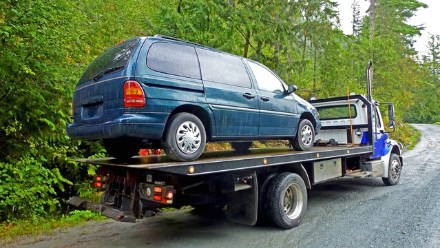 Towing service - the blue tow truck with the loaded old damaged car which stopped working in the middle of forest on the rough off road. Back view