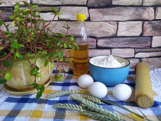 Still life of food on the kitchen table a bowl of flour chicken eggs a bottle of sunflower oil wheat ears a wooden rolling pin indoor flower