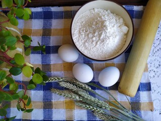 Still life of food on the kitchen table a bowl of flour chicken eggs a bottle of sunflower oil wheat ears a wooden rolling pin indoor flower