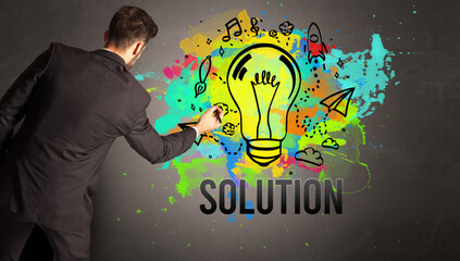 businessman drawing colorful light bulb with SOLUTION inscription on textured concrete wall, new business idea concept