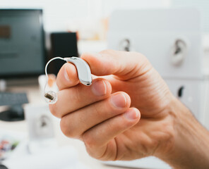 BTE hearing aid close-up in a male hand. Hearing solution, man holds a hearing aid, macro