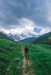 Fototapeta na wymiar Girl traveler with a backpack in the mountains of Georgia. North Caucasus. Walking route to the village of Ushguli. Green valley with wild flowers.