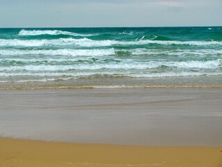 wild beach with beautiful yellow sand and small sea waves with white foam