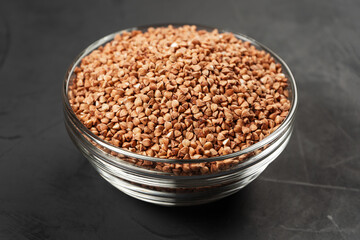 Glass container with buckwheat on a black background in the center of the frame.