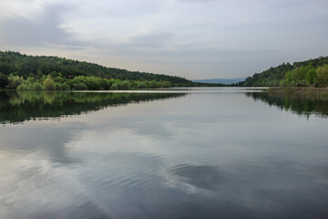 Lake with reflection of green forest in cloudy day landscape