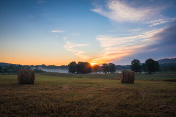 Hay bales rolled on field at sunrise with fog creates amazing sky in early summer Sussex County NJ 