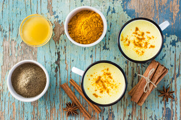 Detox drink. Golden milk with turmeric and cinnamon in mugs and ingredients for cooking on a wooden table. Top view