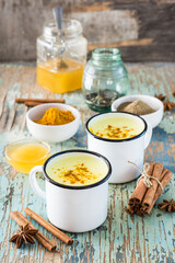 Detox drink. Golden milk with turmeric and cinnamon in mugs and ingredients for cooking on a wooden table. Rustic style