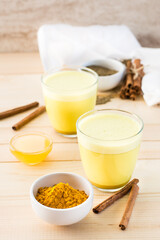 Fototapeta na wymiar Detox drink. Golden milk with turmeric and cinnamon in glasses and ingredients for cooking on a wooden table.
