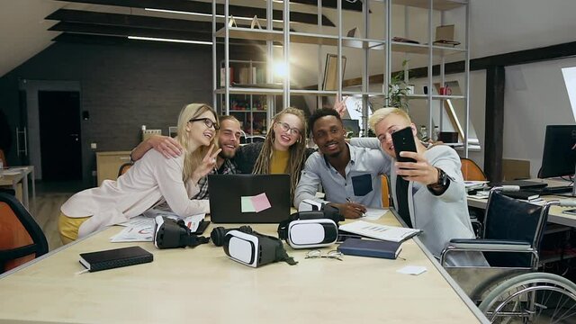 Good-looking happy creative modern young office people making selfie on phone while sitting at the worktable in contemporary office