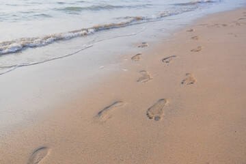 Footprints in the sand at sunset. Beautiful sandy tropical beach with sea waves. Footsteps on the shore.Sea, waves and footprints on the yellow sand on the beach.Soft wave of the sea