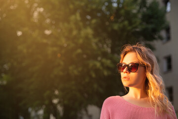 young woman in sunglasses and pink sweater outdoors in the evening. High quality photo