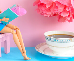 doll reads a book on a pink chair with a Cup of coffee and a pink peony on a pink and blue background, creative concept