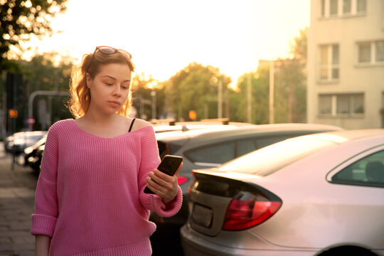 young woman in sunglasses and pink sweater looks at the phone outdoors in the evening. High quality photo