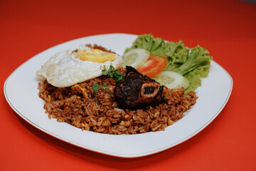 Indonesian fried rice with sunny side up and grilled spare ribs. fresh tomato lettuce and cucumber