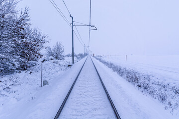 Obraz premium Snow covered train tracks leading into a thick fog. Straight railway tracks leading lines in wintertime
