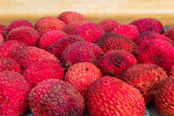 close up of many red lychees on a wooden colored background