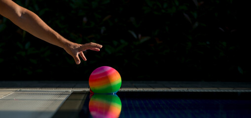 The man is picking up colorful ball from pool