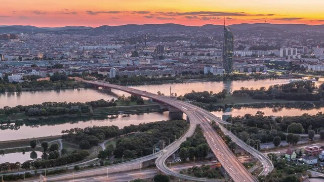 Aerial panoramic view over Vienna city with skyscrapers, highway intersection and a riverside promenade day to night transition timelapse in Austria. Evening skyline after sunset from Danube Tower