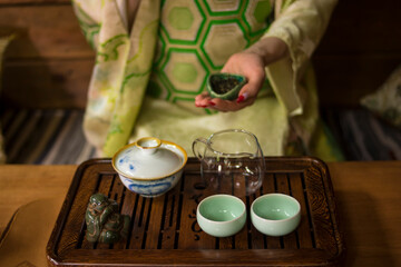 A girl in a Japanese kimono is holding a bowl with Chinese Lujing tea. Table with bowls, a wooden tray, a transparent cup. 
Good for restaurants, tea establishments, banners, posters, flyers.