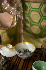A girl in a green kimono pours water from a transparent teapot into a white bowl with tea on a wooden tray. Good for restaurants, banners, posters, flyers.
