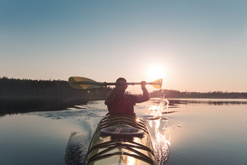 A man is swimming in a kayak. The sun shines behind him.