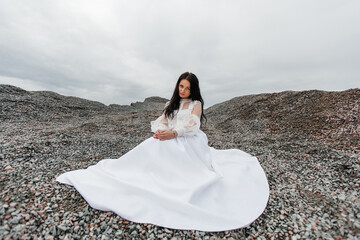  beautiful dreamy brunette in a snow-white puffy dress is sitting on the rocks.