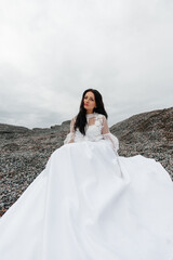 Fototapeta na wymiar beautiful dreamy brunette in a snow-white puffy dress is sitting on the rocks.
