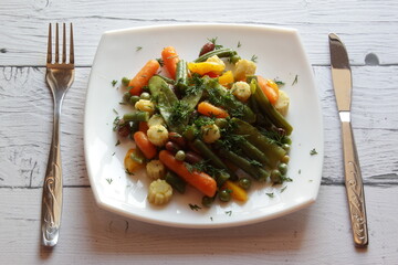 Plate of stir fry vegetables on wooden table. Top view. Summer salad in white plate.
