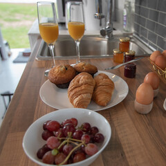 A celebration breakfast is served in this trendy renovated camper van, includes eggs, croissants, orange juice etc served on wooden kitchen surface and grey tiled kitchen area