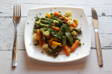 Plate of stir fry vegetables on wooden table. Top view. Summer salad in white plate.