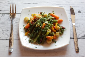 Plate of stir fry vegetables on wooden table. Top view. Summer salad in white plate.