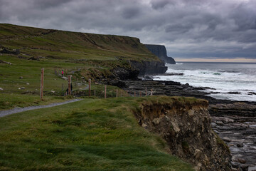 Fototapeta na wymiar Landscape of coastal cliff walk on a stormy, cloudy day with rough sea in Doolin, Co. Clare, Ireland. Wild Atlantic Way.