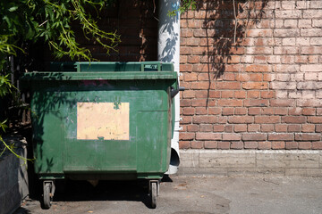 A green dumpster next to a brick wall