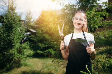 Portrait of a beautiful florist girl in a protective suit who holds garden scissors and shows a...