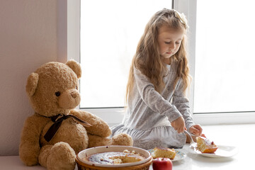 child little girl eating pie on the windowsill with a teddy bear