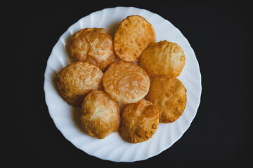 Traditional Indian deep fried poori on white plate with black background top view.