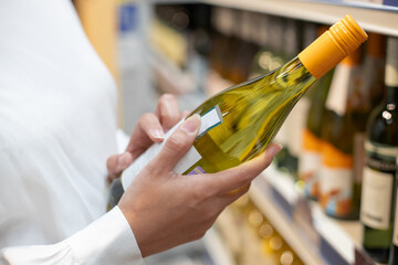 A woman takes alcoholic drinks from the supermarket shelf. Shopping for alcohol in the store.