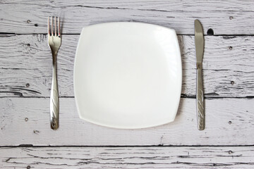 Empty plate, fork and knife over wooden background. Clean plate and cutlery on light background....