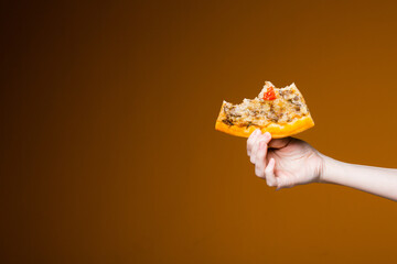 Womans hand on an orange background holding a bitten slice of pizza is like a pizzeria and fast food